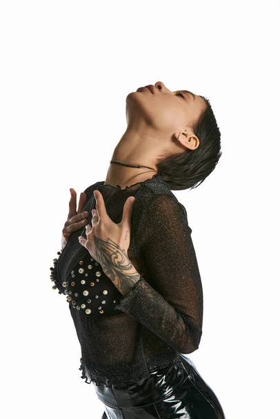 Uma jovem elegante com tatuagens usando uma camisa preta, capturada em um estúdio contra um fundo cinza. - Foto, Imagem