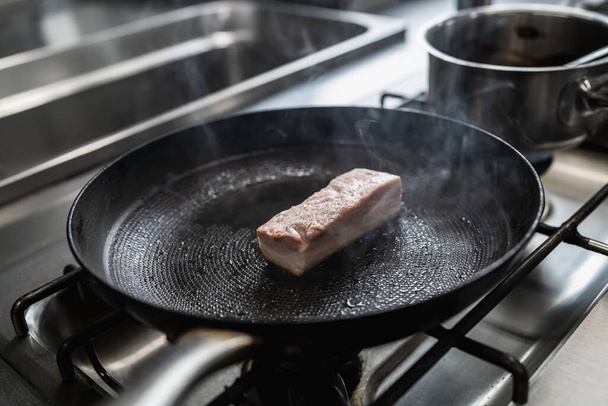 Сырая свинина жаркое в горячей сковороде с маслом на газовой плите в профессиональной кухне в ресторане. Роскошный образ концепции приготовления пищи в отеле. - Фото, изображение