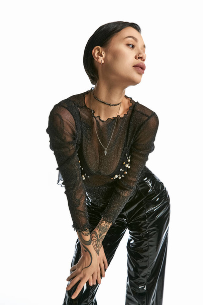 Uma mulher elegante, vestindo um top preto e calças, exala elegância e sofisticação em um cenário de estúdio contra um pano de fundo cinza. - Foto, Imagem