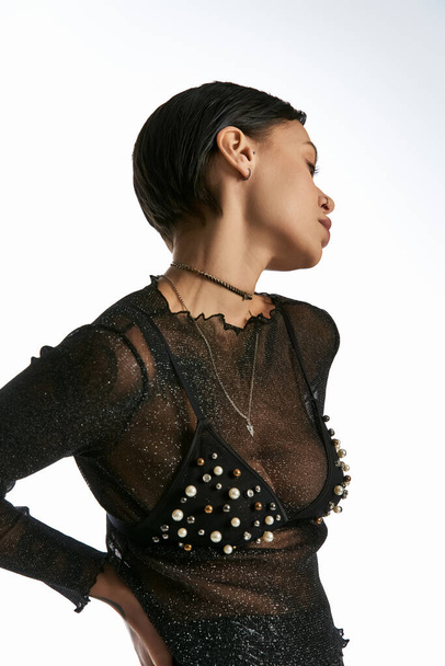 スタジオのセッティングで洗練と優雅さを誇る真珠で覆われた黒いトップに飾られたスタイリッシュな女性. - 写真・画像