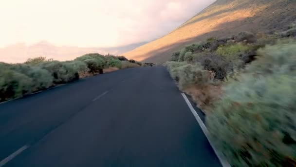 Рух у реальному часі на порожній асфальтній дорозі зі слідами та зеленими кущами дерев на узбіччі Тенеріфе проти білих хмар над горами на вершині сонячного світла - Кадри, відео