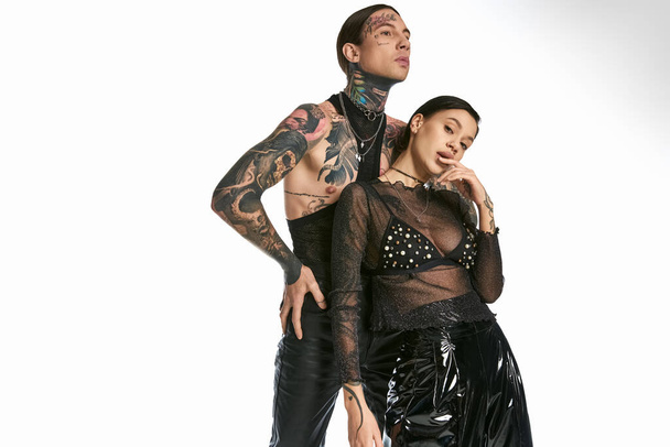 A stylish man with tattoos stands next to a woman in a captivating black dress in a studio against a grey background. - Photo, Image