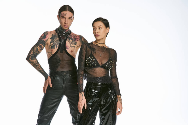 Ένα νεαρό, στιλάτο και με τατουάζ ζευγάρι στέκεται το ένα δίπλα στο άλλο σε ένα στούντιο με γκρι φόντο.. - Φωτογραφία, εικόνα