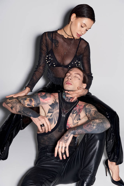 Un uomo e una donna eleganti e tatuati posano in uno studio su uno sfondo grigio. - Foto, immagini