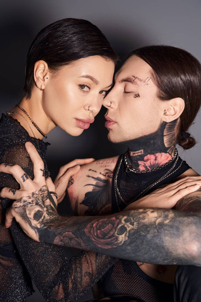 Una pareja elegante y tatuada compartiendo un cálido abrazo en un estudio sobre un fondo gris, expresando amor e intimidad. - Foto, imagen