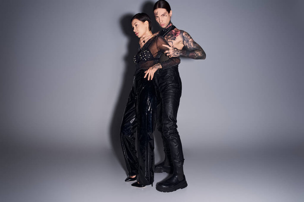 Молодая, стильная и татуированная пара, стоящая вместе в студии на сером фоне. - Фото, изображение