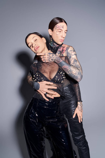 Una pareja joven, elegante y tatuada posando con gracia en un estudio sobre un fondo gris. - Foto, imagen