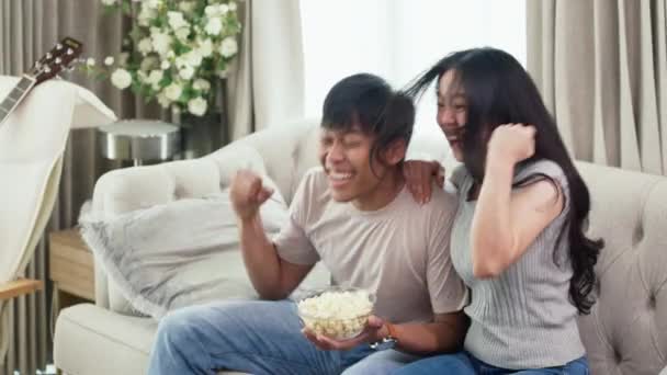 Overjoyed coppia asiatica seduta sul divano e guardando gioco di sport insieme. - Filmati, video