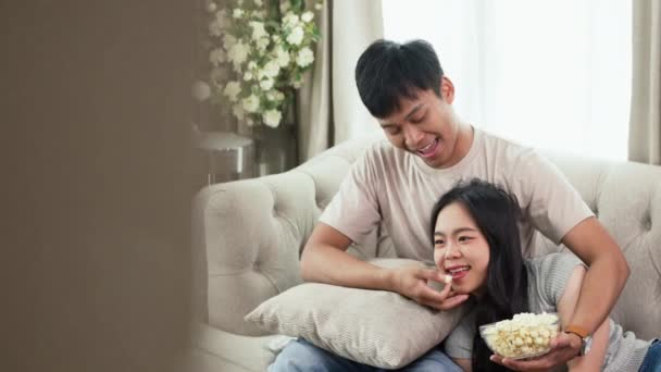 Romanttinen nuori pari rentoutua sohvalla kotona katsomassa televisiota ja syö popcornia. - Materiaali, video