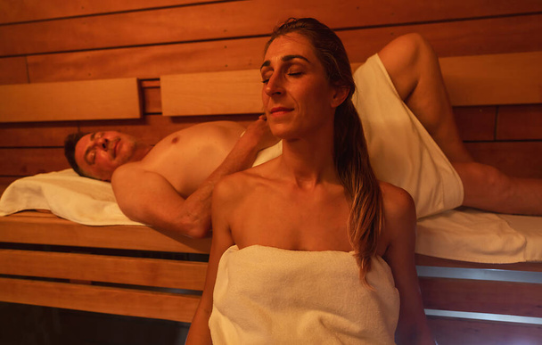 femme et un homme se relaxant dans un sauna finlandais, homme couché en arrière-plan, lumière chaude - Photo, image