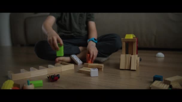 Παιδί παίζει με πολύχρωμα μπλοκ παιχνιδιών οικοδόμηση ενός πύργου κάθεται στο πάτωμα. Εκπαιδευτικό παιχνίδι για το μωρό και το παιδί. Τα παιδιά χτίζουν σπίτι παιχνιδιών - Πλάνα, βίντεο