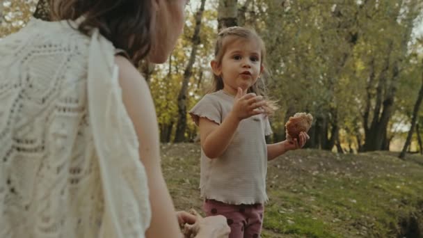 Malá holčička, stojící s matkou u jezera a pojídající krajíc chleba, připravená nakrmit kachny v letním parku. Šťastné dítě baví s pozorováním - Záběry, video
