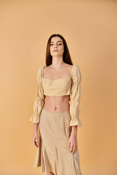 A young woman with long brunette hair strikes a pose in a stylish crop top and skirt, exuding summer vibes in a studio setting. - Photo, Image