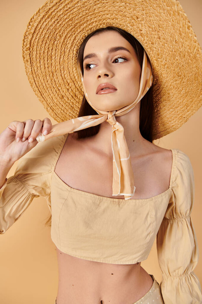 長いブルネットの髪を持つ若い女性がスタジオの設定でポーズを打ち,わら帽子と夏のバイブを除く活気に満ちた黄色のトップを身に着けています. - 写真・画像