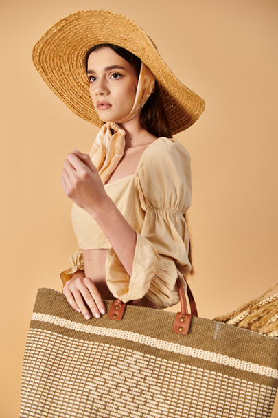 Una joven con el pelo largo y morena posa en un traje de verano mientras sostiene una bolsa marrón y blanca. - Foto, Imagen
