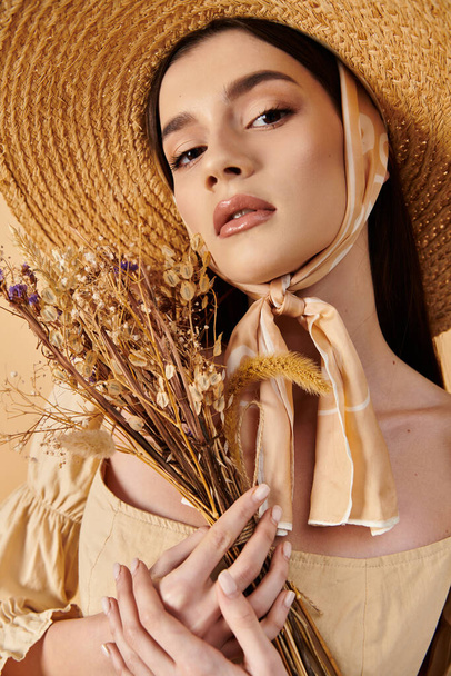 Μια νεαρή γυναίκα με μακριά καστανά μαλλιά ποζάρει με καλοκαιρινό ντύσιμο, φορώντας ψάθινο καπέλο και κρατώντας ένα μπουκέτο λουλούδια. - Φωτογραφία, εικόνα