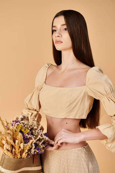A young woman with long brunette hair poses in a crop top, holding a vibrant bouquet of flowers in a studio setting. - Foto, afbeelding