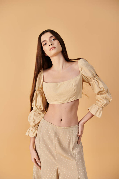 Uzun esmer saçlı genç bir kadın yaz havası yayıyor şık bir bluzla ve geniş bacaklı pantolonuyla, stüdyo ortamında poz veriyor.. - Fotoğraf, Görsel