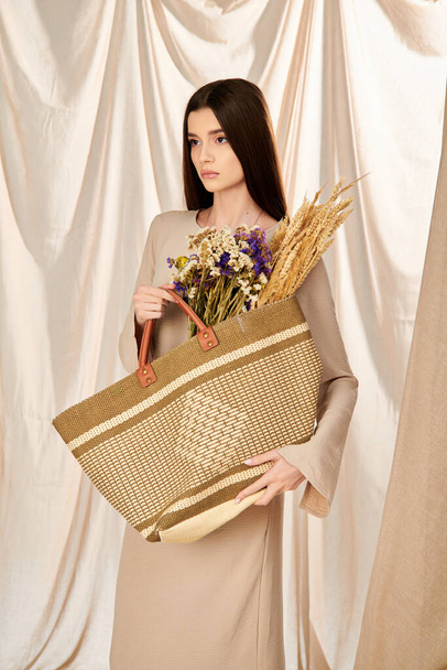Uma jovem com cabelos longos e morena alegremente segura uma cesta transbordando de flores vibrantes, incorporando um humor de verão. Instrução. - Foto, Imagem