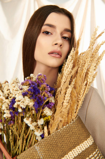Młoda kobieta z długimi brunetkami, emanuje letnią atmosferą, gdy trzyma bukiet suszonych kwiatów w studio. - Zdjęcie, obraz