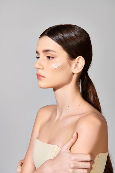 A young woman with brunette hair applying cream on her face, exuding self-love in a studio setting. - Photo, Image