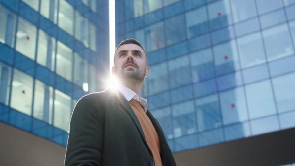 Ένας νεαρός λευκός επιχειρηματίας με επίσημο κοστούμι και γραβάτα στέκεται μπροστά από το κτίριο του χώρου εργασίας. Κάνει μια σοβαρή και εμπνευσμένη χειρονομία καθώς κοιτάζει γύρω του. - Πλάνα, βίντεο
