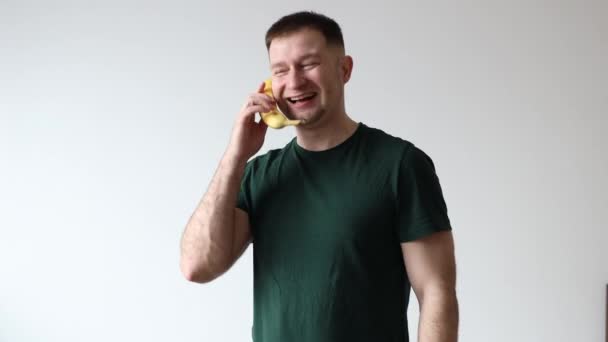 El hombre sostiene el plátano y se comunica en él como teléfono. Las emociones del hombre durante la conversación - Imágenes, Vídeo