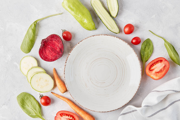 Veganistisch, biologisch, gezond voedsel, plantaardig dieet concept. Witte plaat op tafel tussen groenten en fruit close-up. bovenaanzicht, kopieer ruimte. - Foto, afbeelding