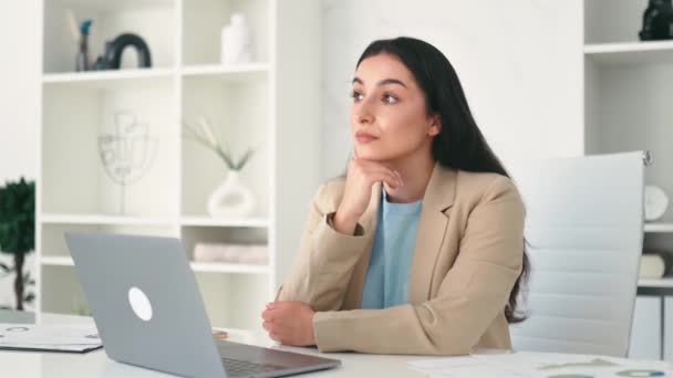 Pensive belle femme d'affaires arabe ou indienne rêveuse réussie, PDG d'entreprise, avocat d'entreprise, assis au bureau dans le bureau créatif moderne regardant loin et pensant à quelque chose - Séquence, vidéo