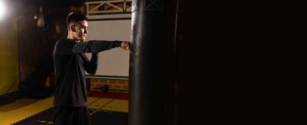 Hombre joven boxeador golpeando un saco de boxeo en un club de boxeo. Hombre guapo boxeador entrenando duro. Banner. Copiar espacio - Foto, imagen