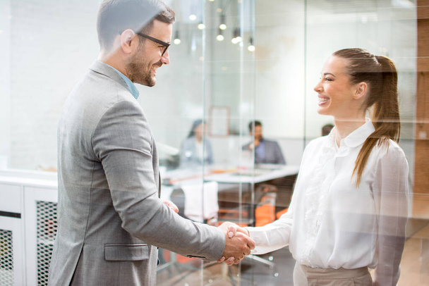 Young attractive business woman and handsome businessman shaking hands indoors - Photo, Image