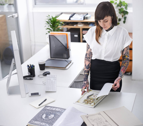 Tattoo, woman and book in office for business with creative planning, design choice and sketch in folder. Entrepreneur, artist and ring binder with inspiration for body art and work project at desk. - Photo, Image