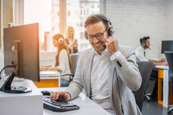 Lächelnder Geschäftsmann am Telefon mit Headset im Gespräch mit dem Kunden - Foto, Bild