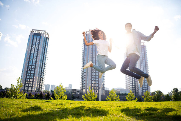 Full body length photo of overjoyed young couple wearing casual outfit jumping bought apartments in new residential complex on background. - Foto, imagen