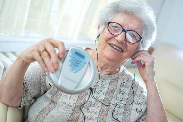 Cheerful grandmother listening to music on mp3 player at home - Photo, Image
