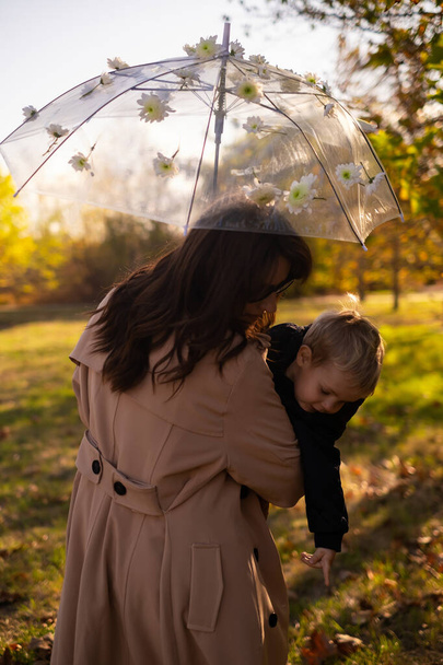 Bir anne ve oğlu bahar parkında geziniyor. Kadın çiçekli bir şemsiye tutuyor. Parkta bir aile yürüyüşü, aile hafta sonları, aileler günü ya da anneler günü için mükemmel.. - Fotoğraf, Görsel