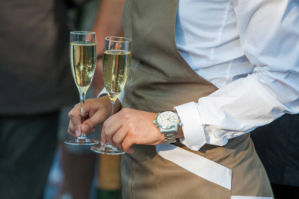 Een moment van feest wordt vastgelegd in deze close-up met twee handen die fluiten van sprankelende champagne vasthouden, klaar voor een toast. Een hand is versierd met een verfijnd polshorloge, suggereert een formele - Foto, afbeelding