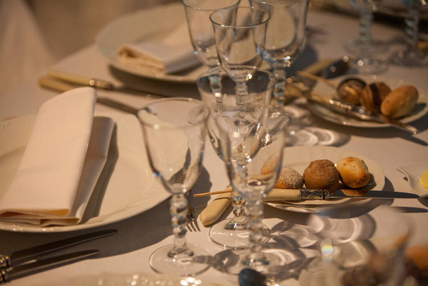 Eine Nahaufnahme eines raffinierten Speisesaals mit kristallklaren Gläsern, elegantem weißen Geschirr und fein gefalteten Servietten. Abgerundet wird das einladende Arrangement mit einer Auswahl an frisch gebackenen - Foto, Bild