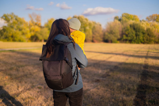 Een vrouw met een rugzak reist met haar zoon, genietend van een familiewandeling in het bos. Ze omarmen een actieve levensstijl, sportieve wandeluitrusting en verkennen milieuvriendelijk toerisme. - Foto, afbeelding