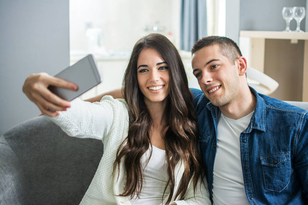 Νεαρό ζευγάρι παίρνει μια selfie με έξυπνο τηλέφωνο στο σπίτι - Φωτογραφία, εικόνα