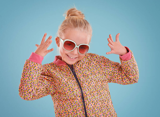 Little girl, portrait and fashion with sunglasses in studio for trendy, cool and funky style with confidence. Cute child, smile and happy in blue background, young kid and retro clothes with glasses. - Photo, Image