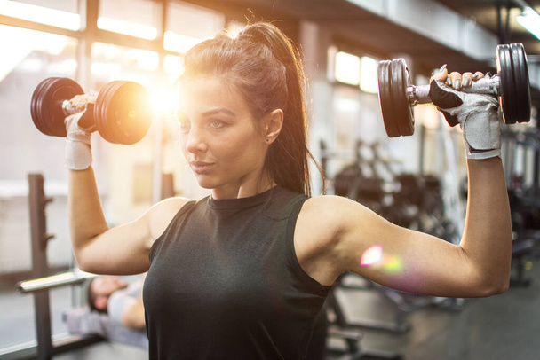 Gyönyörű fiatal nő edz súlyzókkal az edzőteremben - Fotó, kép