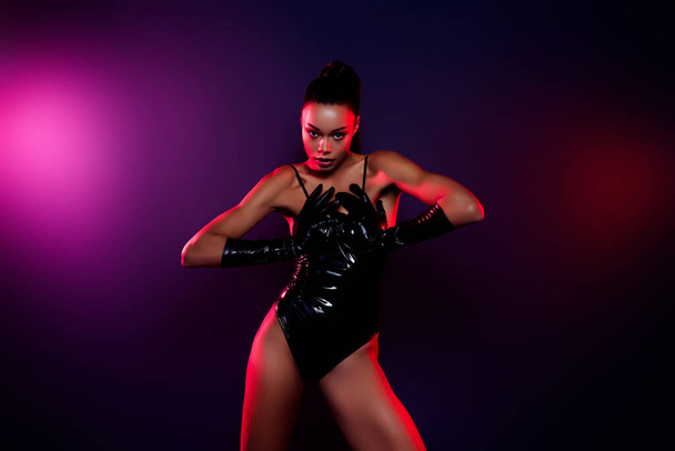 Kuva afrikkalainen amerikkalainen tyttö laittaa kädet rinnassa musta nahka puku poseeraa eristetty kaltevuus neon tausta. - Valokuva, kuva