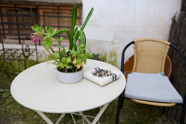 Csendélet egy fehér asztalnál székkel a kertben. Hamutartó cigarettacsikkekkel az asztalon. A tüdőbetegségek fogalma. Tüdőrák-tudatossági kampány - Fotó, kép