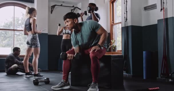 A többnemzetiségű fiatal férfi súlyzózik, miközben a tornateremben ül. Kiváló minőségű 4k felvételek - Felvétel, videó