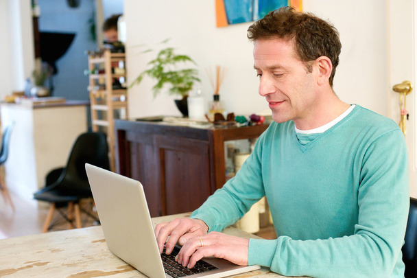 Dojrzały dorosły samiec siedzi przy stole w domu za pomocą laptopa  - Zdjęcie, obraz