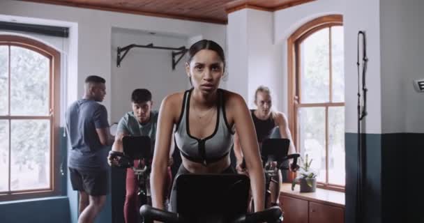 Grupa osób ćwiczy na rowerach stacjonarnych na siłowni, otoczona przez wyposażenie wnętrz i sprzęt sportowy - Materiał filmowy, wideo