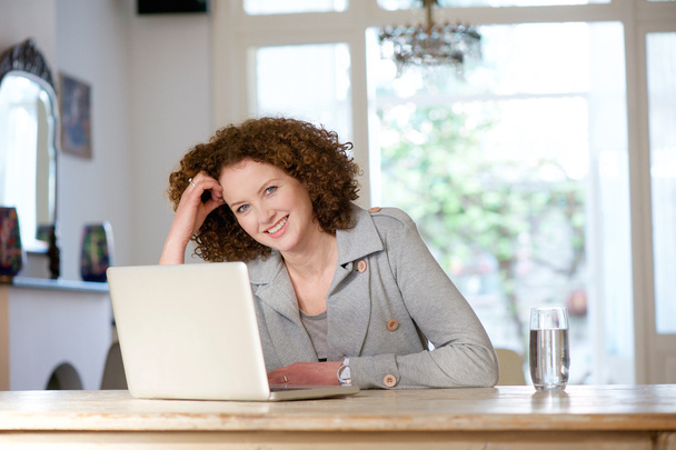 Uśmiechający się starsza kobieta siedzi w tabela przy użyciu laptopa - Zdjęcie, obraz