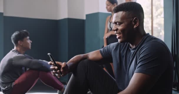 Африканец улыбается мобильнику в фитнес-студии. Высококачественные 4k кадры - Кадры, видео