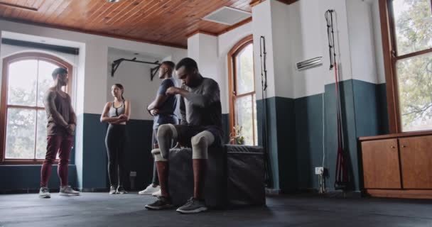 Různorodá skupina v tělocvičně, včetně muže s protetickou nohou a dalšího s kolenním podpěrou, se navzájem inspirují ve fitness aktivitách, projevují podporu a inkluzivitu - Záběry, video